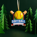 Load image into Gallery viewer, Personalized softball Christmas ornament featuring a yellow softball with stitched details and crossed bats design on a shield style background, customizable name area on the front banner and customizable year area on the softball, glossy finish with raised 3D front details and flat 2D back, white hanging ribbon, displayed on a snowy softball field themed holiday background with pine branches and festive decorations.