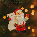 Load image into Gallery viewer, Decorative Christmas ornament of Santa Claus holding a 'Nice List' sign with blurred lights in the background.