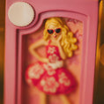 Load image into Gallery viewer, A vibrant pink fashion doll ornament with a retro camera-frame look and floral dress, perfect for holiday trees. Features bright colors, playful style, and a customizable area for adding a name or short text. Designed as a fun keepsake for kids and collectors who love bold, glamorous ornaments. Ideal for Christmas décor, stocking stuffers, and memorable seasonal gifting.