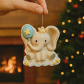 Load image into Gallery viewer, Decorative elephant ornament with a crown and balloon held by a hand against a festive background.
