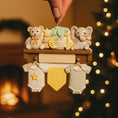 Load image into Gallery viewer, Decorative ornament with teddy bear, elephant, and baby clothes on a wooden stand against a warm, blurred background.