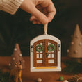 Load image into Gallery viewer, Hand holding a small decorative door with wreaths, surrounded by festive elements like a deer and Christmas trees.