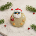 Load image into Gallery viewer, Decorative ornament with Santa Claus design on a marble surface with Christmas decorations.