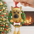 Load image into Gallery viewer, Dog Christmas ornament with a wreath and Santa hat, held by a hand with a festive background.