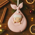 Load image into Gallery viewer, Pink baby-shaped ornament on a wooden surface with cinnamon sticks and dried oranges.
