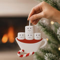 Load image into Gallery viewer, Decorative ornament shaped like a teacup with smiling marshmallows and a candy cane, held by a hand against a festive background.