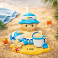 Load image into Gallery viewer, Personalized Beach Baby Christmas Ornament featuring a cheerful toddler sitting on the sand with a beach hat, float, bucket, and shovel. This detailed 3D front design includes raised elements, bright summer colors, and textured sand base for added depth. The name is placed on the hat and the year on the sandy base. A perfect keepsake for baby’s first beach trip or summer memory, ideal for Christmas tree decor or a thoughtful holiday gift for new parents.