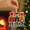 Load image into Gallery viewer, Colorful nutcracker Christmas ornament held by a hand with a festive background.