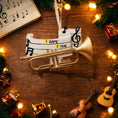 Load image into Gallery viewer, Personalized music ornament featuring a white musical staff design with black notes and a gold trumpet detail. Includes free handwritten personalization with one name and year written on the sheet music. Shown hanging with a ribbon in a warm festive holiday setting with soft lights instruments and seasonal decor. Designed with a 3D raised front and flat back perfect for Christmas tree display and gifts for musicians music lovers and band members.