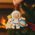 Load image into Gallery viewer, Personalized astronaut Christmas ornament featuring a detailed 3D front design with a smiling space explorer holding a colorful planet and bright yellow stars. The childâs name is added on the suit and the year is written on the star for a custom touch. This space themed ornament is perfect for kids who love rockets, planets, and outer space dreams. A fun and meaningful holiday keepsake for future astronauts and little space lovers.