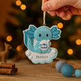 Load image into Gallery viewer, Decorative ornament with a blue axolotl character and personalized text, held against a festive background.