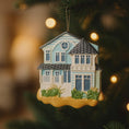 Load image into Gallery viewer, House-shaped Christmas ornament on a tree with blurred lights in the background