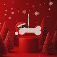 Load image into Gallery viewer, Personalized dog Christmas ornament featuring a bone shaped design with a glitter red Santa hat detail on one end, customizable name area centered on the ornament and customizable year displayed on the opposite side, smooth glossy finish with glitter accents, flat lightweight structure and red hanging ribbon, photographed on a snowy holiday styled background with pine branches, festive Christmas ornaments, dog themed props, and warm seasonal lighting for pet lovers.