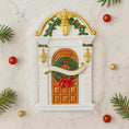 Load image into Gallery viewer, Decorative Christmas door ornament with gold accents, red bow, and greenery on a light background.