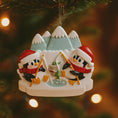 Load image into Gallery viewer, Christmas ornament with two penguins ice fishing on a mountain background, hanging on a tree.