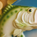 Load image into Gallery viewer, Decorative Bass fish ornament held by a hand with a blurred Christmas tree in the background