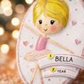 Load image into Gallery viewer, Personalized ballet girl Christmas ornament featuring a cute ballerina character in a pink tutu dress with heart details, customizable name area on the front banner and customizable year area below, glossy finish with raised 3D front details and flat 2D back, white hanging ribbon, displayed on a snowy holiday background with pine branches and festive decorations.