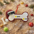 Load image into Gallery viewer, Personalized dog Christmas ornament featuring a bone shaped design with a glitter red Santa hat detail on one end, customizable name area centered on the ornament and customizable year displayed on the opposite side, smooth glossy finish with glitter accents, flat lightweight structure and red hanging ribbon, photographed on a snowy holiday styled background with pine branches, festive Christmas ornaments, dog themed props, and warm seasonal lighting for pet lovers.