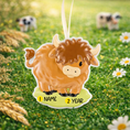 Load image into Gallery viewer, Adorable Highland cow themed Christmas ornament featuring a fluffy brown cow design with soft rounded details and a warm countryside feel. Styled in a natural green meadow setting, this ornament is designed to be personalized and brings a cozy farm inspired charm to holiday tree decor.