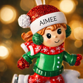 Load image into Gallery viewer, This ice skating girl ornament features a joyful winter character gliding on ice, wearing a festive red and green outfit with cozy winter details. The design highlights a playful skating pose, soft facial expression, and winter accessories that capture the magic of the holiday season. Personalized with a name on the hat and a year on the ice base, this ornament works beautifully as a Christmas tree decoration or winter keepsake gift for children and families.