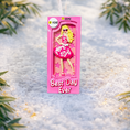 Load image into Gallery viewer, A vibrant pink fashion doll ornament with a retro camera-frame look and floral dress, perfect for holiday trees. Features bright colors, playful style, and a customizable area for adding a name or short text. Designed as a fun keepsake for kids and collectors who love bold, glamorous ornaments. Ideal for Christmas décor, stocking stuffers, and memorable seasonal gifting.