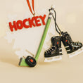 Load image into Gallery viewer, Hockey-themed ornament with 'HOCKEY' text, hockey stick, and skates on a beige background