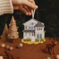 Load image into Gallery viewer, Hand holding a miniature house ornament with Christmas decorations in the background