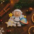 Load image into Gallery viewer, Personalized astronaut Christmas ornament featuring a detailed 3D front design with a smiling space explorer holding a colorful planet and bright yellow stars. The childâs name is added on the suit and the year is written on the star for a custom touch. This space themed ornament is perfect for kids who love rockets, planets, and outer space dreams. A fun and meaningful holiday keepsake for future astronauts and little space lovers.