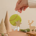 Load image into Gallery viewer, Hand holding a green ornament with a star and white details against a beige background with Christmas decorations.