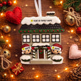 Load image into Gallery viewer, Personalized Christmas house ornament featuring a cozy winter home decorated with snow, wreaths, garlands, and festive details. Two smiling characters wearing Santa hats peek from the front, each customizable with a name, while the roof displays a year or family name. Designed with a detailed 3D raised front and smooth finish, this ornament is perfect for Christmas tree decor, family keepsakes, new home celebrations, and holiday gifting.