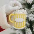 Load image into Gallery viewer, Yellow mug ornament held by a gloved hand with a blurred Christmas tree background