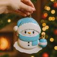 Load image into Gallery viewer, Personalized Snowman Baby Christmas Ornament featuring a cheerful snowman with blue glitter hat and scarf, holding a sparkling ornament. This design has a raised 3D front with textured details, dimensional elements, and vibrant winter colors. The child’s name is placed on the scarf and the year is added below. A perfect keepsake for baby’s first Christmas, newborn gift, winter holiday decoration, and meaningful family tree memory ornament.
