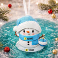 Load image into Gallery viewer, Personalized Snowman Baby Christmas Ornament featuring a cheerful snowman with blue glitter hat and scarf, holding a sparkling ornament. This design has a raised 3D front with textured details, dimensional elements, and vibrant winter colors. The child’s name is placed on the scarf and the year is added below. A perfect keepsake for baby’s first Christmas, newborn gift, winter holiday decoration, and meaningful family tree memory ornament.