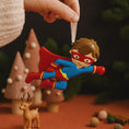 Load image into Gallery viewer, Superhero ornament being hung on a Christmas tree with festive background
