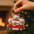Load image into Gallery viewer, Polar bear family in a red car Christmas ornament held by a hand with a festive background.