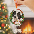Load image into Gallery viewer, Dog Christmas ornament with a wreath, held by a hand against a festive background.