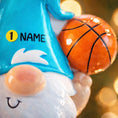 Load image into Gallery viewer, Personalized basketball gnome Christmas ornament featuring a cute blue gnome character holding a basketball, customizable name area on the hat and customizable year area on the base, glossy finish with raised 3D front details and flat 2D back, white hanging ribbon, displayed on a snowy holiday background with pine branches and festive decorations.