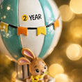 Load image into Gallery viewer, A personalized baby boy ornament featuring a cute bunny riding a pastel blue hot air balloon. Soft blue and white tones with gentle decorative details create a calm and cozy look. Handwritten personalization includes baby name and year. Mostly 2D ornament with raised 3D details on the front only, lightweight and easy to hang, perfect for baby first Christmas, nursery decor, and toddler keepsakes.