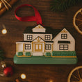 Load image into Gallery viewer, House-shaped Christmas ornament on a wooden surface with festive decorations.