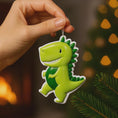 Load image into Gallery viewer, Personalized dinosaur Christmas ornament with a raised 3D front featuring a cute green dinosaur design and glossy detailed texture. The ornament has a flat 2D back for easy hanging and durability. Bright green color, playful smile, and sculpted spikes create a fun and eye catching look. Hand personalized with name and year. Perfect kids Christmas ornament, dinosaur themed holiday decor, and personalized keepsake gift.