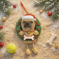 Load image into Gallery viewer, Dog-shaped Christmas ornament with a wreath, Santa hat, and bone tag on a sandy background with ornaments.