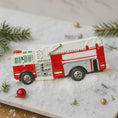 Load image into Gallery viewer, Fire truck-shaped ornament on a snowy surface with Christmas decorations