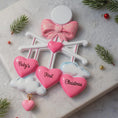 Load image into Gallery viewer, Personalized Baby Girl First Christmas Ornament featuring a dimensional 3D front design with pink glitter bow, heart charms, and hanging cloud detail. The baby’s name is added on the top circle and the year on the cloud, creating a meaningful keepsake. Soft pink tones, layered hearts reading Baby’s First Christmas, and festive holiday accents make it perfect for newborn girl gifts, baby shower presents, and treasured Christmas tree memories.
