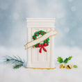 Load image into Gallery viewer, Decorative Christmas wreath with a red bow on a white pedestal against a snowy background.