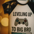 Load image into Gallery viewer, ornament Shirt with 'Leveling Up to Big Bro' text and gaming controller graphic on a blurred background