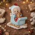 Load image into Gallery viewer, Personalized baby first Christmas ornament featuring a sweet baby boy sitting in a pastel blue sleigh holding a small teddy bear. Handwritten baby name and year displayed on the sleigh front. Smooth resin finish with soft winter tones, lightweight structure, mostly 2D ornament with raised 3D front details, designed for baby boy nursery themed Christmas tree decor and keepsake gifting.