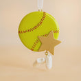 Load image into Gallery viewer, Decorative ornament shaped like a softball with a star and shoe charm on a beige background