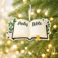 Load image into Gallery viewer, Personalized Holy Bible Christmas Ornament featuring an open scripture design with elegant “Holy Bible” lettering across the pages. The left page is customized with a name and the right page displays the year, creating a meaningful faith based keepsake. Surrounded by soft greenery and delicate flowers, this religious ornament is perfect for baptisms, baby dedications, first communions, or celebrating a Christ centered Christmas. A thoughtful spiritual gift for families who cherish their faith.