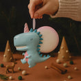 Load image into Gallery viewer, Unicorn-shaped keychain held by a hand with decorative background