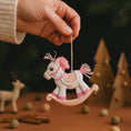 Load image into Gallery viewer, Hand holding a small rocking horse ornament with a dark background